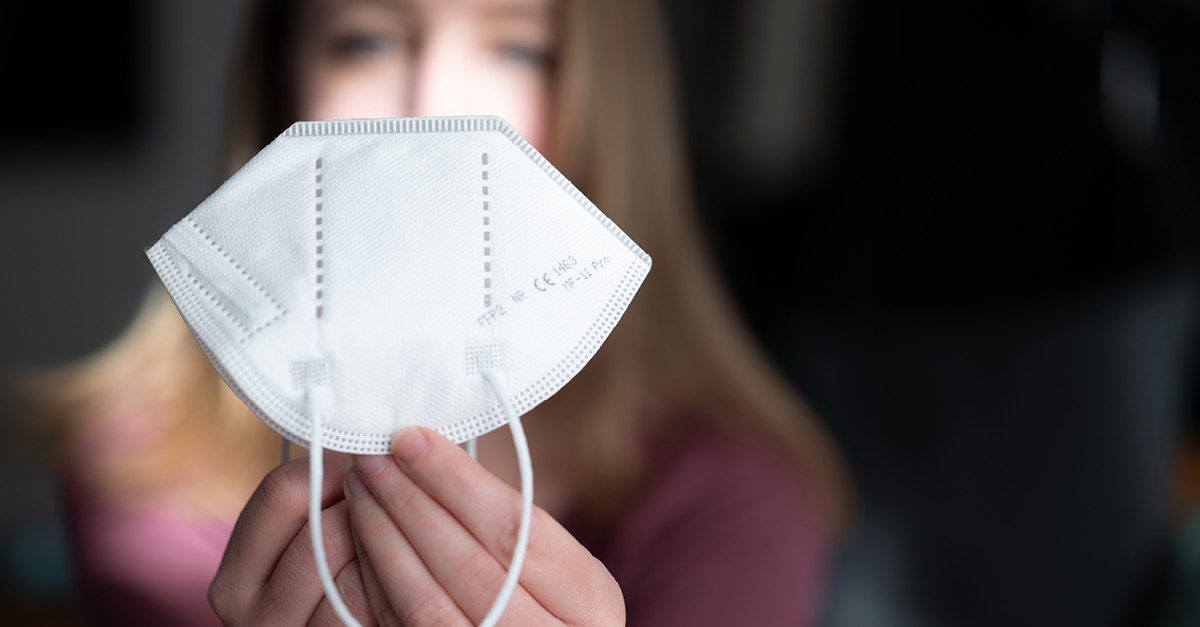 Junge Frau hält FFP2 Maske in der Hand