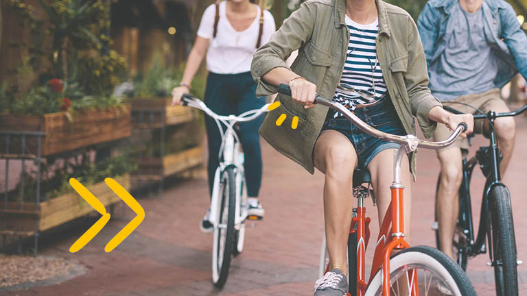 Drei Studierende fahren mit dem Fahrrad in kurzer Hose durch die Stadt