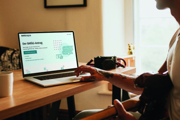 Junge Person sitzt am Schreibtisch und arbeitet am Laptop. Die BAföG Digital Website ist offen.