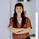 Portrait von Jaqueline Himpler, sie steht mit verschränkten Armen an eine Wand gelehnt.