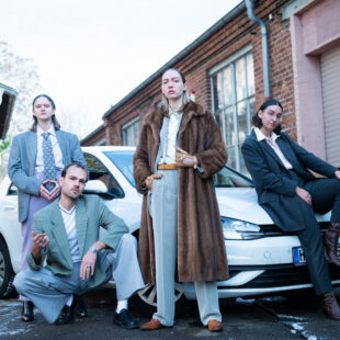 A group of young people in suits are posing in front of a car.