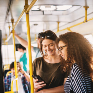 Zwei Frauen schauen in einer Straßenbahn auf ein Handy.