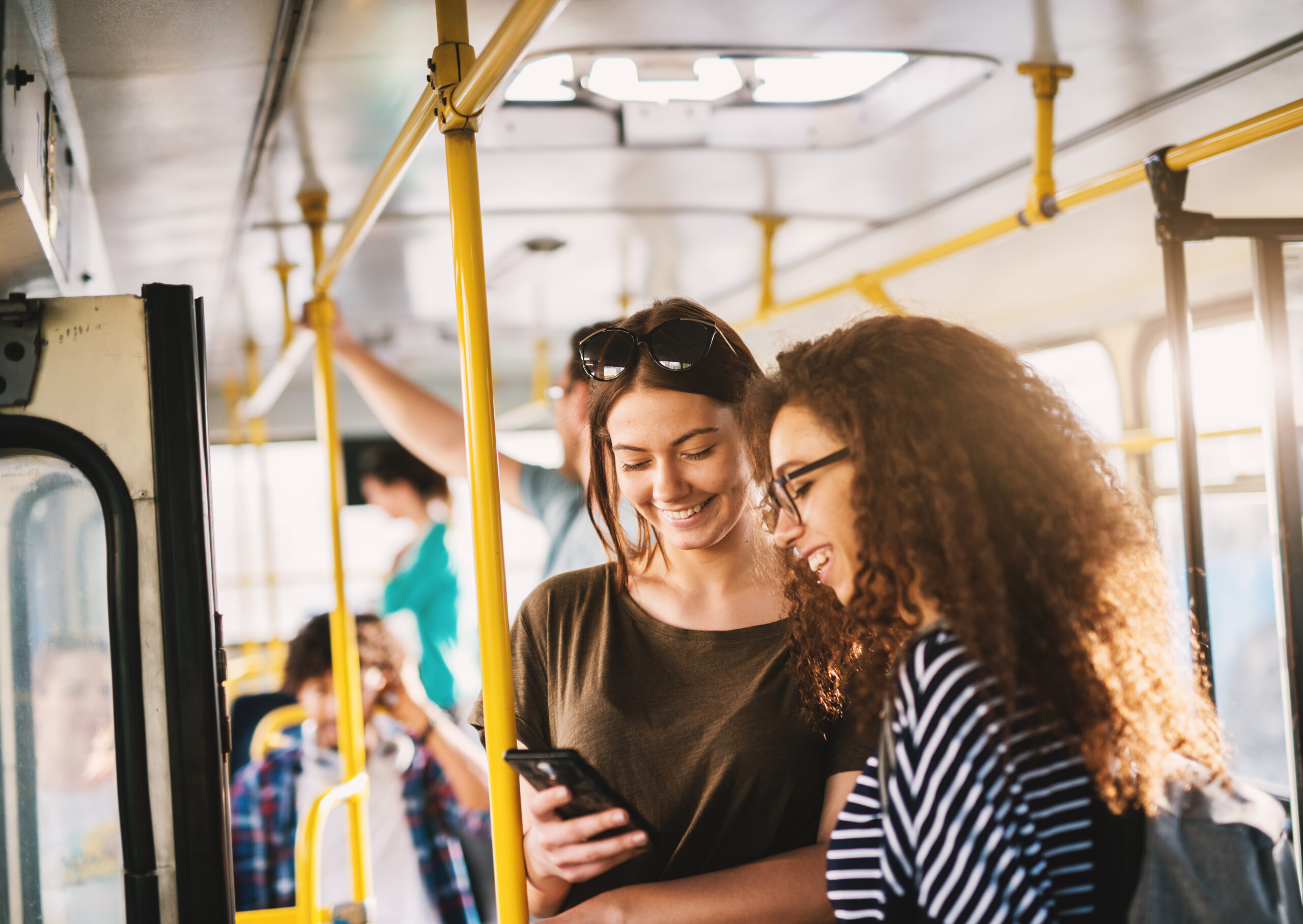 Zwei Frauen schauen in einer Straßenbahn auf ein Handy.