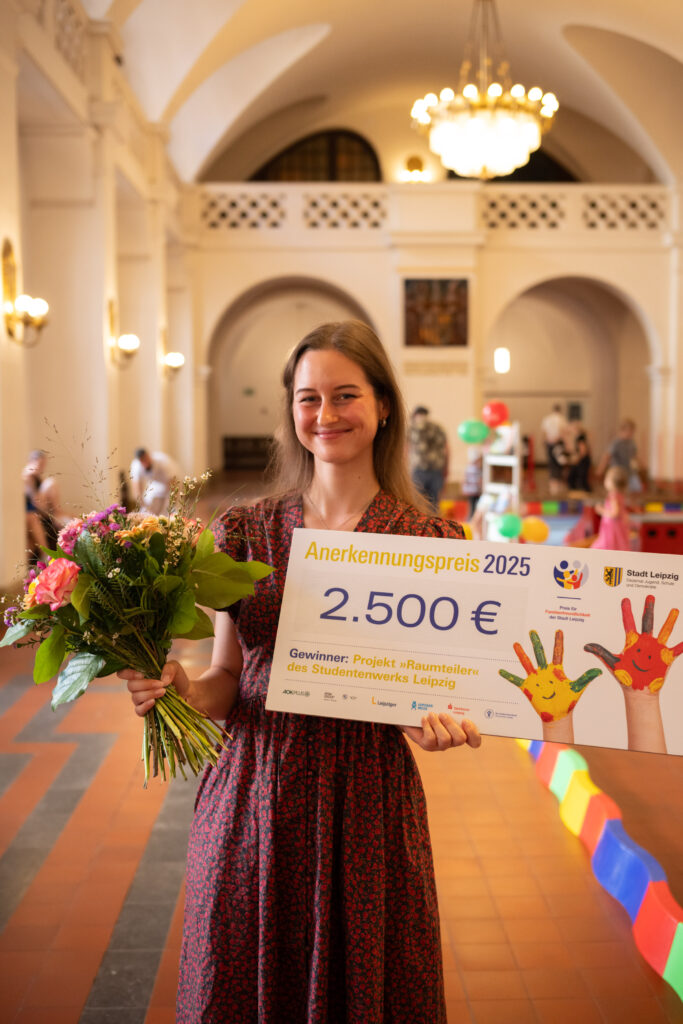 Celina Bohmann, Projektleiterin RaumTeiler, mit Blumenstrauß und Spendenscheck in den Händen beim Familienfreundlichkeitspreis 2025 im Neuen Rathaus der Stadt Leipzig
