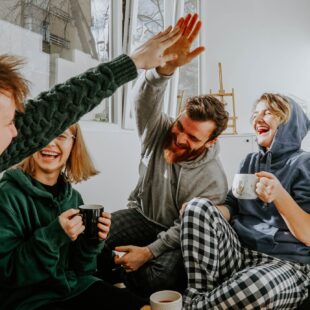 Vier Studierende, die zusammen lachend auf der Coach sitzen und Tee trinken.