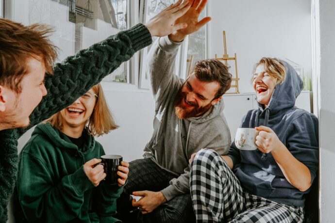 Vier Studierende, die zusammen lachend auf der Coach sitzen und Tee trinken.