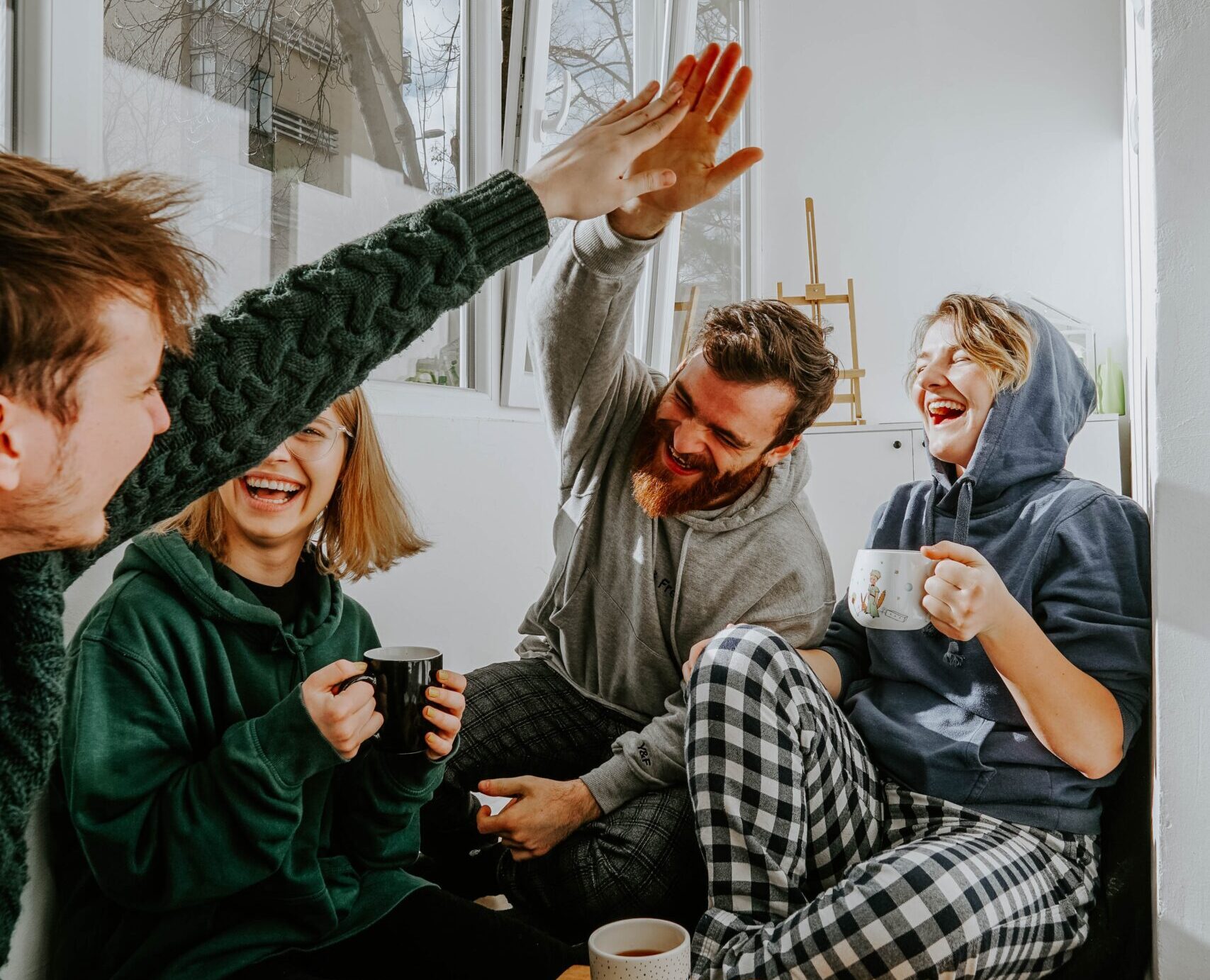 Vier Studierende, die zusammen lachend auf der Coach sitzen und Tee trinken.