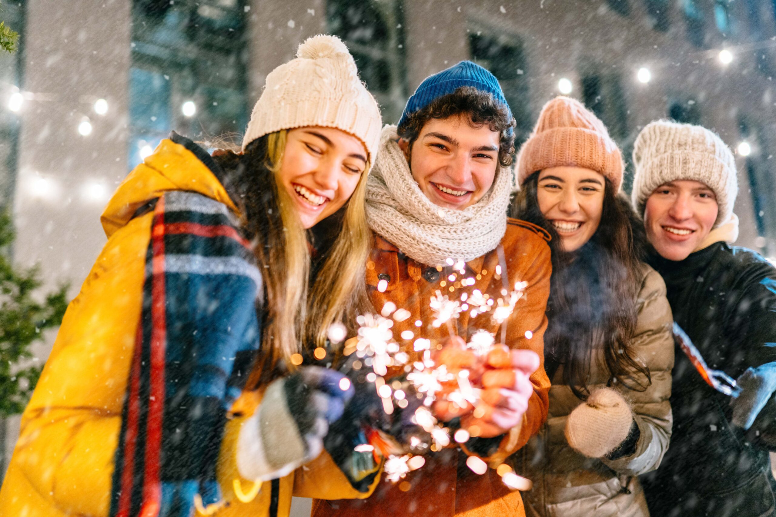 Vier Studierende in warmen Winterkleidern stehen draußen, es schneit und halten Wunderkerzen.