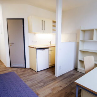 Studentenwohnheim mit Blick auf Eingangsbereich, Küche, Regale, Schreibtisch und Bett