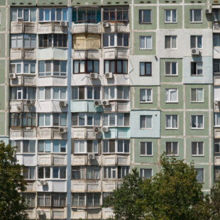 Mehrfamilienhaus mit Balkonen, Klimaanlagen und Bäumen im Vordergrund.