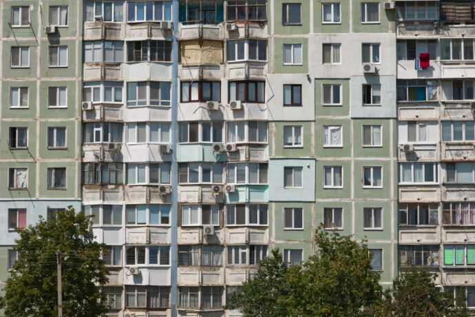 Mehrfamilienhaus mit Balkonen, Klimaanlagen und Bäumen im Vordergrund.
