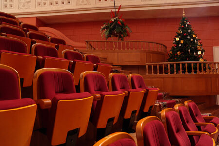 Leerer Theatersaal mit roten Stühlen, an der Seite der Sitzplätze ist ein Weihnachtsbaum aufgestellt